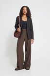 Model met een zwarte blazer, zwart topje, wijde bruine broek en bruine schoenen.