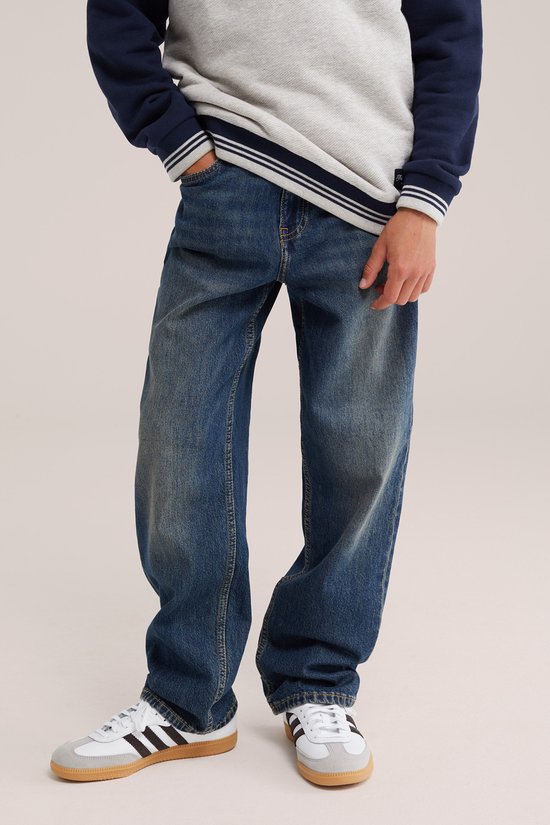 Jongen in donkerblauwe loose fit jeans en gestreepte trui, close-up op de pasvorm.