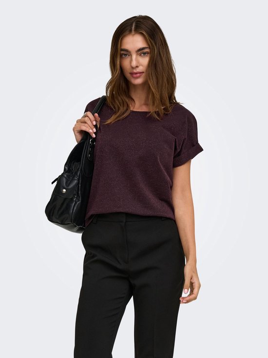 Model draagt donkerpaarse top met korte mouwen en glitterdetails, zwarte broek en zwarte tas.
