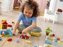 Une petite fille joue avec des blocs LEGO DUPLO, une voiture et un château sur le sol.