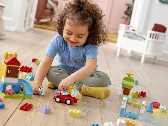 Une petite fille joue avec des blocs LEGO DUPLO, une voiture et un château sur le sol.