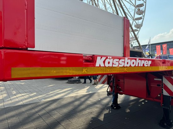 Rode aanhanger met witte tekst 'Kässbohrer' en gele reflecterende streep.