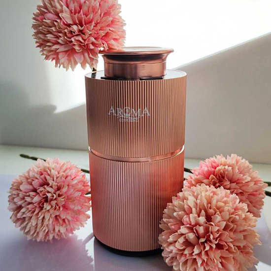Koperkleurige, geribbelde Aroma diffuser omringd door roze pluizige bloemen.