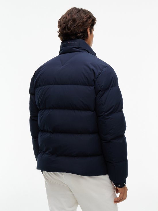 Achteraanzicht van een man in een donkerblauwe gewatteerde jas met logo bij de kraag.