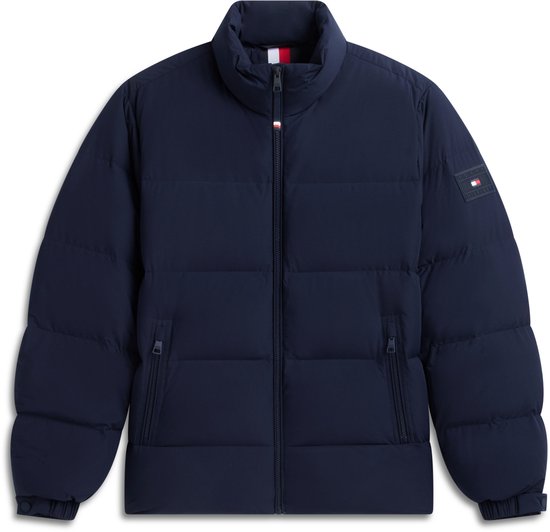 Donkerblauwe gewatteerde jas met Tommy Hilfiger-logo op de mouw, plat op een witte achtergrond.