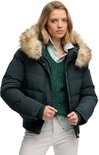 Vrouw met blond haar, draagt een donkergroene bomberjack met bontkraag, groene kabeltrui en gestreepte blouse. Het jack heeft een ritssluiting en drukknopen.