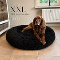 Bruine hond op een ronde, zwarte, pluizige hondenmand van 100 cm.