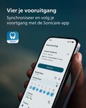 Hand die een smartphone vasthoudt met de Philips Sonicare app, die poetsgegevens toont.