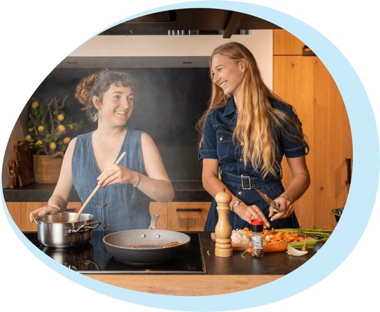 Twee vrouwen koken in een keuken, een vrouw roert in een pan, de ander snijdt wortels.