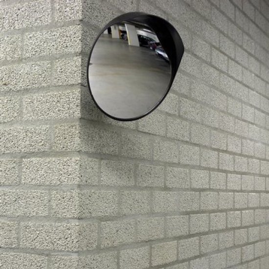 Miroir de sécurité rond de 30 cm de diamètre, monté sur un mur en briques grises. Le miroir a un bord noir et un support de fixation en métal.