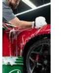 Man wast een rode auto met schuimend autoshampoo.
