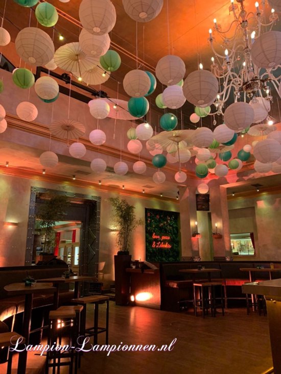 Een restaurant interieur met veel witte en groene lampionnen en parasols aan het plafond. Sfeervolle verlichting.