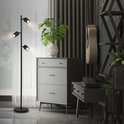 Zwarte staande lamp met drie verstelbare spots, in een woonkamer met meubels.
