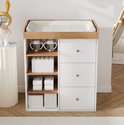 Witte commode met houten accenten, drie laden met gouden knoppen en drie open planken.