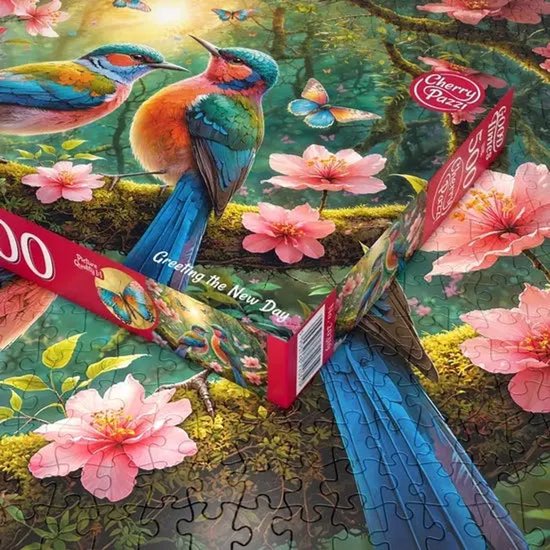 Een groot deel van een 500-stukjespuzzel, "Greeting the New Day", met twee kleurrijke vogels, bloemen en vlinders, met delen van de puzzeldoos.