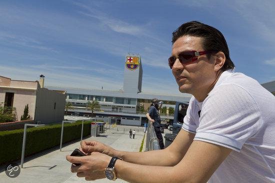 Man met zonnebril kijkt naar de verte, met een stadion van FC Barcelona op de achtergrond.