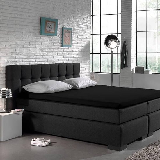 Een tweepersoonsbed met een zwart hoeslaken en een knoppenkop.