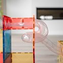Doorzichtige gebogen buizen vormen een spiraal en verbinden rode en gele magnetische tegels in een opstelling.