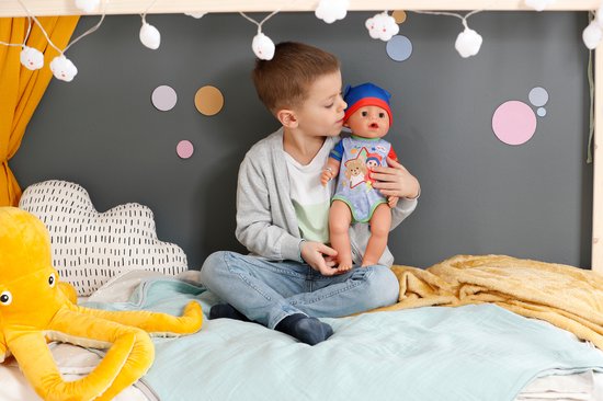 Jongen houdt BABY born pop vast in bed. Pop draagt blauwe muts en romper.