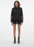 Model in een zwarte geborduurde sweater en zwarte denim shorts.