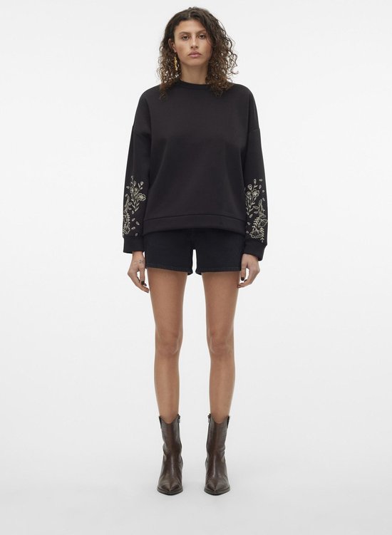 Model in een zwarte geborduurde sweater en zwarte denim shorts.