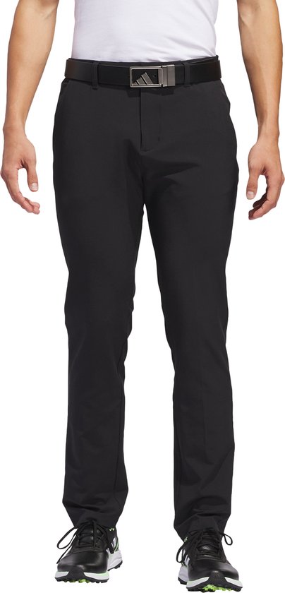 Man in zwarte golfbroek met Adidas-riem en sneakers.