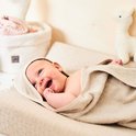 Lachende baby gewikkeld in een beige badcape, met het capuchongedeelte over het hoofdje.