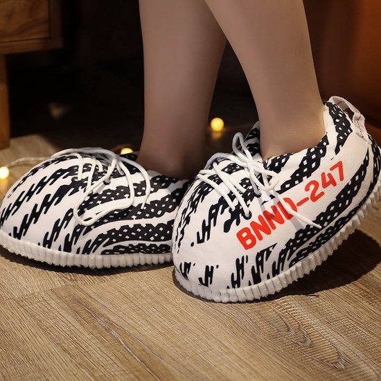 Voeten in zwart-witte sneaker-pantoffels met witte veters en rode BNND-247 opdruk.