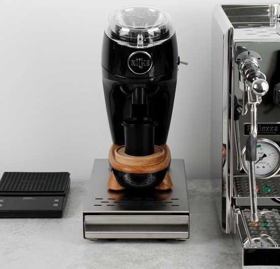 Een zwarte koffiemolen met houten accenten op een zilverkleurige uitklaplade, naast een espressomachine.