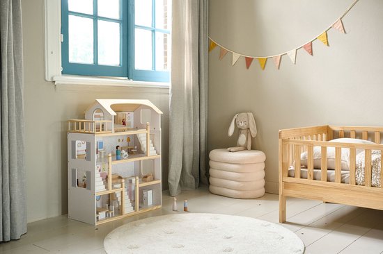 Houten poppenhuis in lichte kleuren, naast een houten ledikant en een ronde witte vloerkleed.