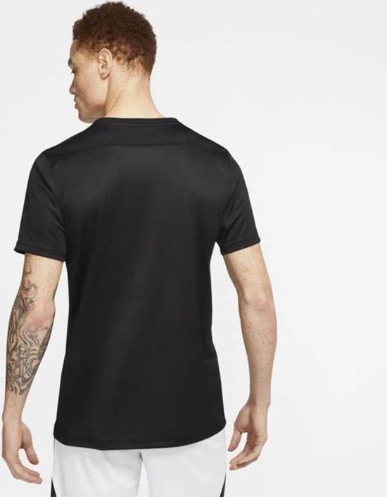 Homme aux cheveux roux avec tatouage sur le bras, vu de dos, portant un t-shirt de sport noir et un short blanc.