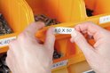 Handen plaatsen een label met '8.0 X 50' op een oranje bakje.