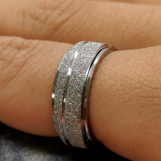 Zilverkleurige ring met een glinsterende, gestreepte band, gedragen op een vinger.