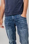Man in een donkerblauw T-shirt en een stonewashed blauwe jeans met extra naden op de bovenbenen.