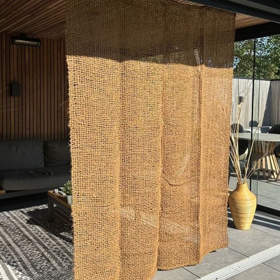 Lichtbruin buitengordijn van kokosvezel, 100x210 cm, met grove weving. Hangt voor een overdekt terras met loungebank.