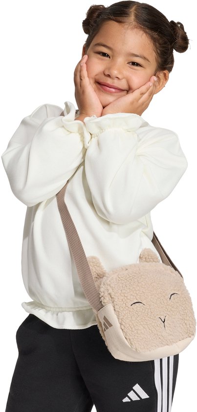 Meisje met een beige teddy tasje in de vorm van een schaapje, draagt een witte trui en zwarte broek.