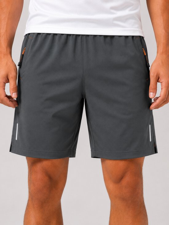 Grijze sportbroek met elastische tailleband, oranje ritsen aan de zijkanten en reflecterende strepen.