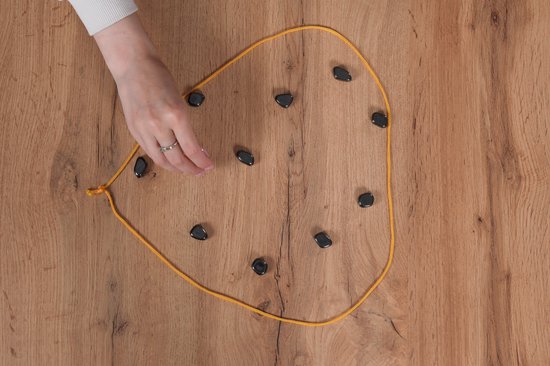 Een hand met een ring plaatst een magneet op een gele lijn op een houten tafel.