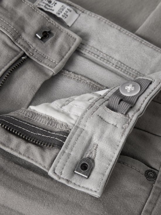Detail van de tailleband van een grijze jeans, met verstelbare knoopsluiting en rits.
