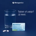 Een glas water, twee witte tabletten en een sachet MetaRelax (smaak lemon/citroen) liggen op een donkere achtergrond. Tekst: Tablet of zakje? Jij kiest.