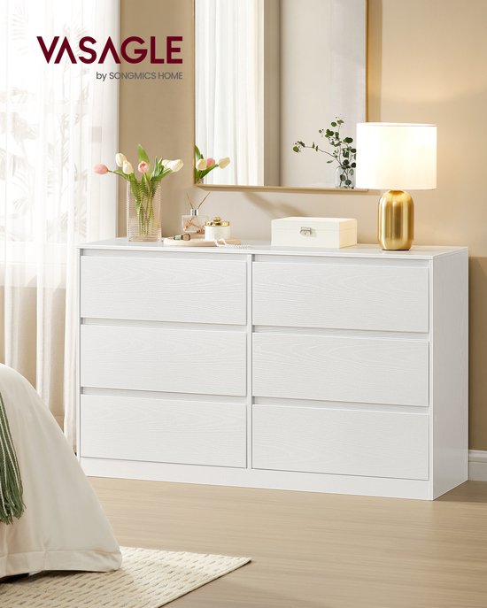 Commode blanche à 6 tiroirs, présentée à côté d'un lit et avec des décorations sur le dessus.
