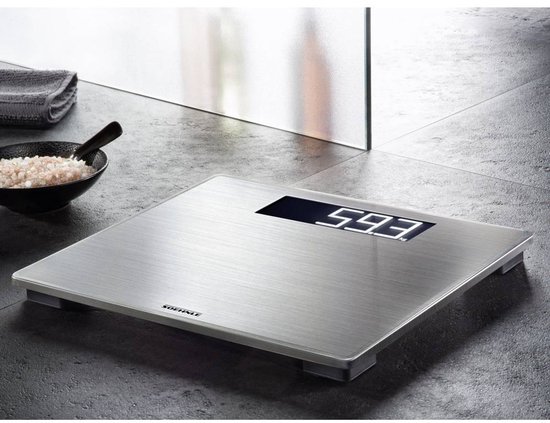 Zilverkleurige weegschaal met digitaal display, '593' weergegeven. Staat op een donkere tegelvloer.