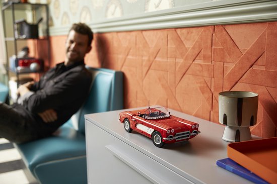 Een man zit op een bankje in een retro diner en houdt een rode LEGO Chevrolet Corvette cabriolet vast. De auto staat op een kast.