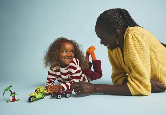 Een vrouw en een kind spelen met LEGO-voertuigen en -figuren op een blauwe achtergrond.