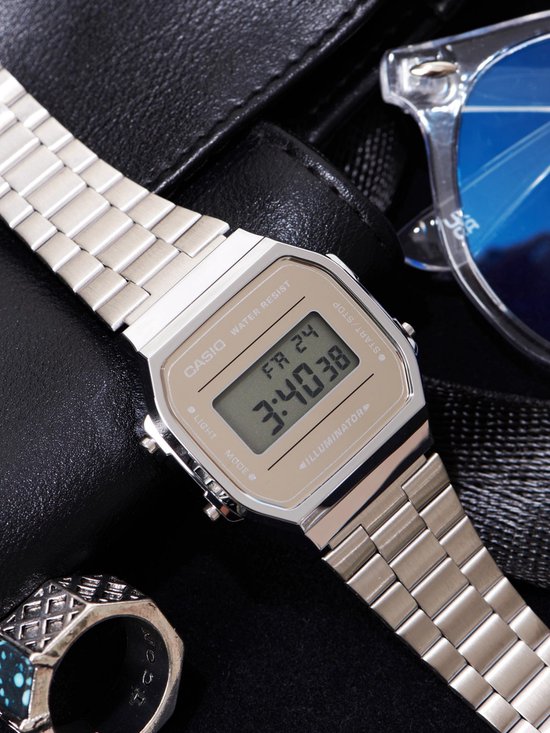 Zilverkleurig Casio horloge met metalen band, om de pols gedragen met een zwarte achtergrond en zonnebril.