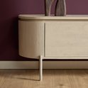Zijkant van een zandkleurig houten tv-meubel met één gebogen deur en één pootje, op een paarse muur.
