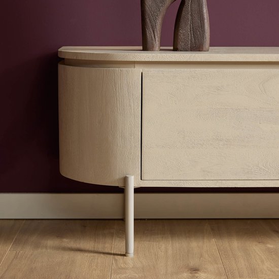 Zijkant van een zandkleurig houten tv-meubel met één gebogen deur en één pootje, op een paarse muur.