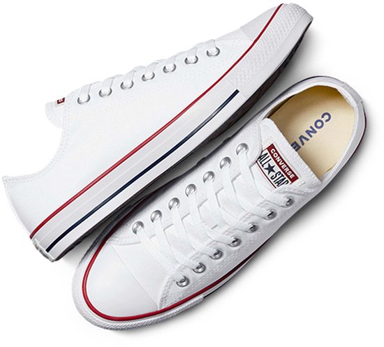 Witte lage Converse sneakers met rode en blauwe strepen op de zool. Een schoen ligt bovenop de ander.