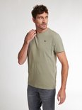 Man met groen t-shirt met korte mouwen en een ronde hals, die aan de kraag trekt.