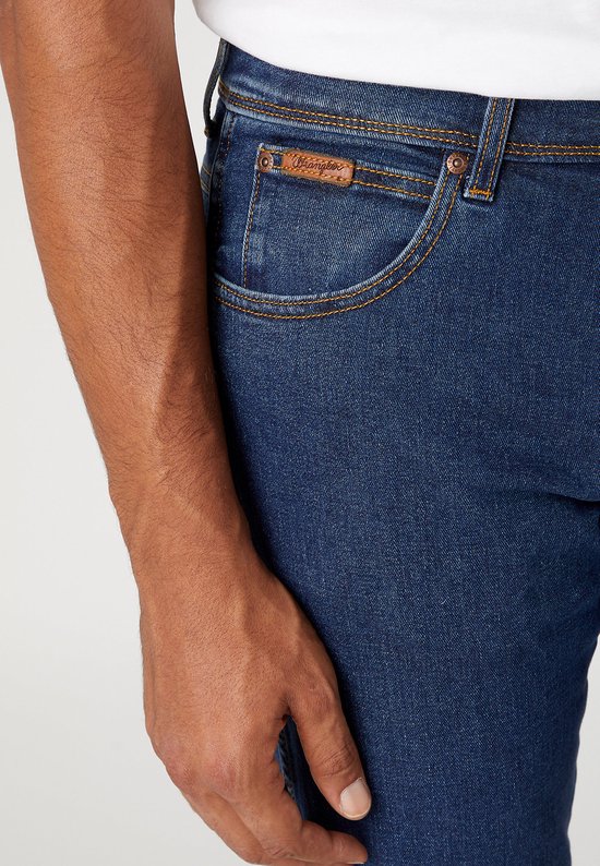 Close-up van een donkerblauwe Wrangler jeans met een bruin label.